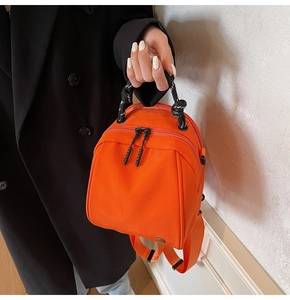 Close-up of stylish orange shell-shaped mini backpack with a black knotted handle strap