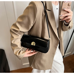 Detail of black patent leather underarm bag with gold arched buckle on camel blazer