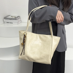 Detalle de bolso tote grande color crema en piel suave con colgante de nudo tejido