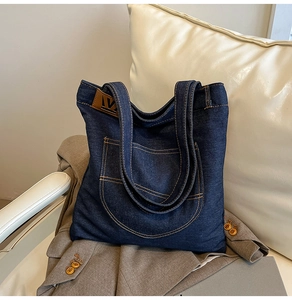 Detail of blue denim tote bag featuring front pocket and brown leather brand patch