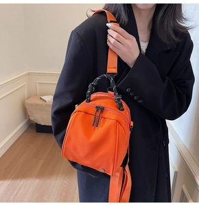 Detail van een oranje nylon mini rugzak met een geweven knoopgreep en zilveren beslag