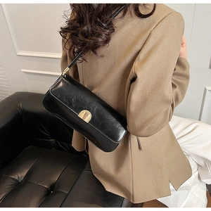 Detail of black underarm bag with gold clasp paired with a professional brown suit
