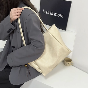 Detalle de un bolso tote grande de cuero crema con cordón trenzado sobre traje gris