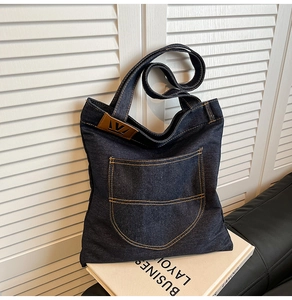 Detail of dark blue denim tote bag featuring orange contrast stitching and leather logo