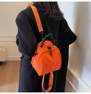 Model met een feloranje mini-rugzak met zwart geweven handvat gedragen over een zwarte jas