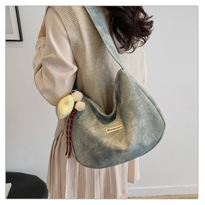 Detail of grey-blue corduroy hobo bag with yellow chick plush pendant and side label