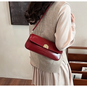 Detail view of red glossy leather underarm bag with gold metal clasp on a model