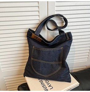 Detail of dark blue denim tote bag with yellow contrast stitching and leather logo patch