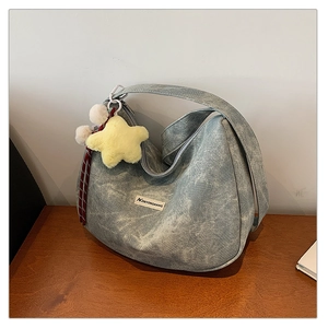 Detail of blue denim hobo bag with yellow star plush charm on a wooden surface
