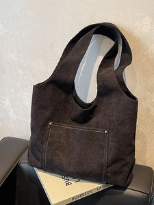 Minimalist black corduroy tote bag with front pocket and contrast stitching on dark sofa