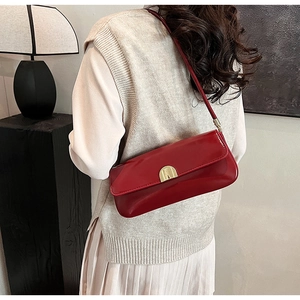 Detail view of red glossy patent leather underarm bag with gold semicircular buckle closure
