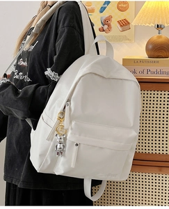 Close-up of white nylon backpack with silver bear charm shown in a cozy indoor setting