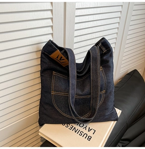 Detail of blue denim tote bag featuring brown leather strap and contrast yellow stitching