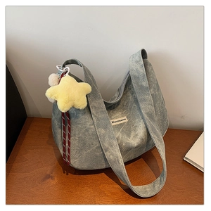 Detail of greyish-blue corduroy hobo bag featuring a yellow plush star charm and wide strap