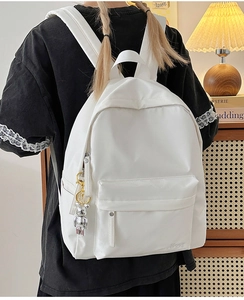 Detail of white nylon backpack with a silver bear charm and branded HOOZ logo
