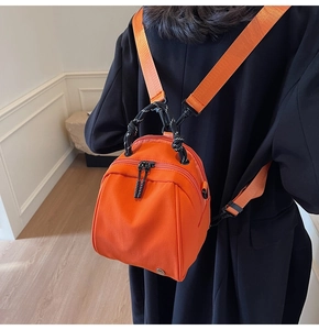 Detail view of mini orange nylon shell bag with decorative woven rope handle on black coat