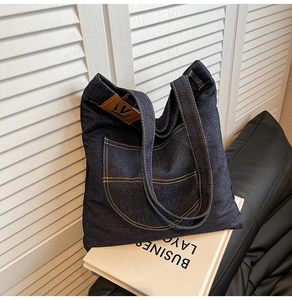 Detail of dark blue denim tote bag with contrast stitching and leather logo patch