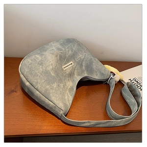 Close-up of light blue washed denim hobo bag with zip closure and plush ball charm