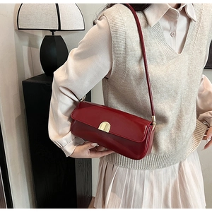 Detail of burgundy glossy leather underarm bag featuring a gold semicircular buckle lock