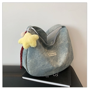 Detail of light blue denim half-moon bag featuring a star pendant and textile logo tag