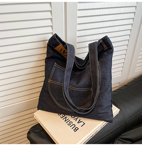 Detail of dark blue denim tote bag with contrast yellow stitching and leather logo label