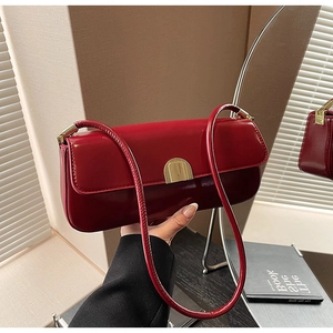 Side view of burgundy patent leather underarm bag with gold clasp held by a model