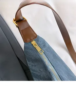 Detailed close-up of blue denim shoulder bag with brown leather strap and gold zipper