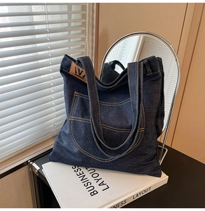Detail of dark blue denim tote bag with orange stitching and leather logo on a book