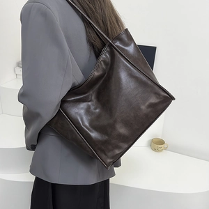 Detalle de un bolso tote grande de cuero café llevado al hombro por una modelo