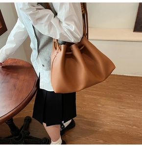 Brown lychee leather bucket bag with drawstring closure shown on shoulder of a model