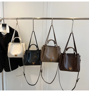 Détail de quatre sacs seaux avec logo triangle en métal dans plusieurs coloris élégants
