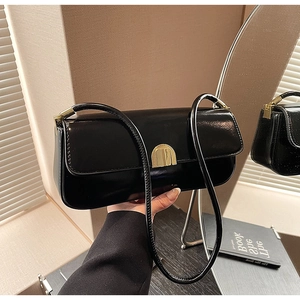 Detail of black glossy leather shoulder bag with elegant gold arch buckle hardware
