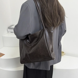 Detalle de bolso tote marrón oscuro en cuero brillante sobre un traje gris de mujer