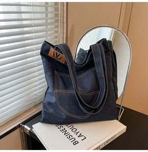 Detail of dark blue denim tote bag with orange stitching and brown leather V-logo patch