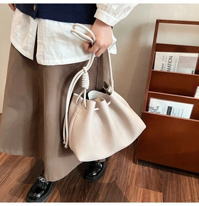 Beige drawstring bucket bag with textured leather and knot detail on a model