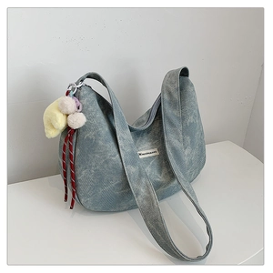 Close-up of light blue washed denim dumpling bag with plush charms and brand label