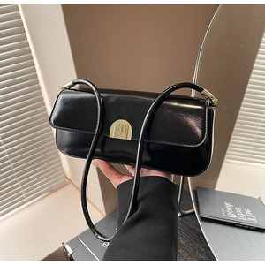 Detail view of black patent leather underarm bag featuring a golden semi-circle metal clasp