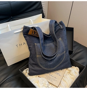 Detail of dark blue denim tote bag with vintage pocket design and leather logo tag