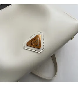 Détail d'un sac seau en cuir blanc cassé avec plaque logo triangulaire dorée vintage