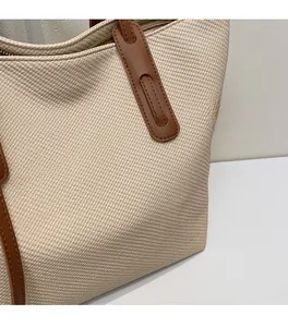 Close-up of off-white canvas tote bag texture with brown leather strap and fine stitching