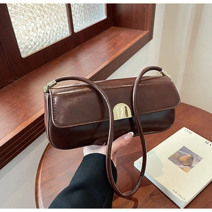 Detail of a brown glossy leather underarm bag with a gold metal clasp on a wooden table