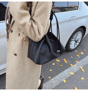 Close-up of black pleated bucket bag with lychee grain texture worn by a model in a coat