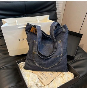 Detailed view of dark denim tote bag with yellow contrast stitching and leather brand logo