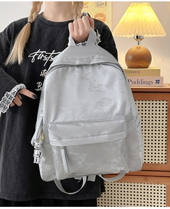 Close-up of light gray floral jacquard backpack with metal bear charm and Hoog logo