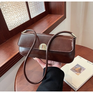 Detail of deep brown oil wax leather baguette bag with golden buckle on a wooden table