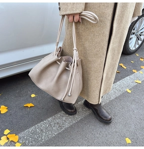 Detail of beige pleated bucket bag with knotted rope strap and metallic sphere accents