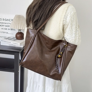 Detalle del bolso tote vintage marrón con nudo trenzado y charm de campana metálica
