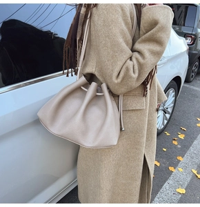Detail of beige pleated bucket bag in lychee leather worn with a khaki wool coat