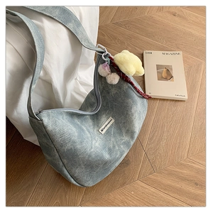 Detail of light blue textured shoulder bag with plush bear charm on wooden floor