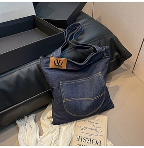 Detailed view of deep blue denim tote bag with leather logo tag and contrast stitching